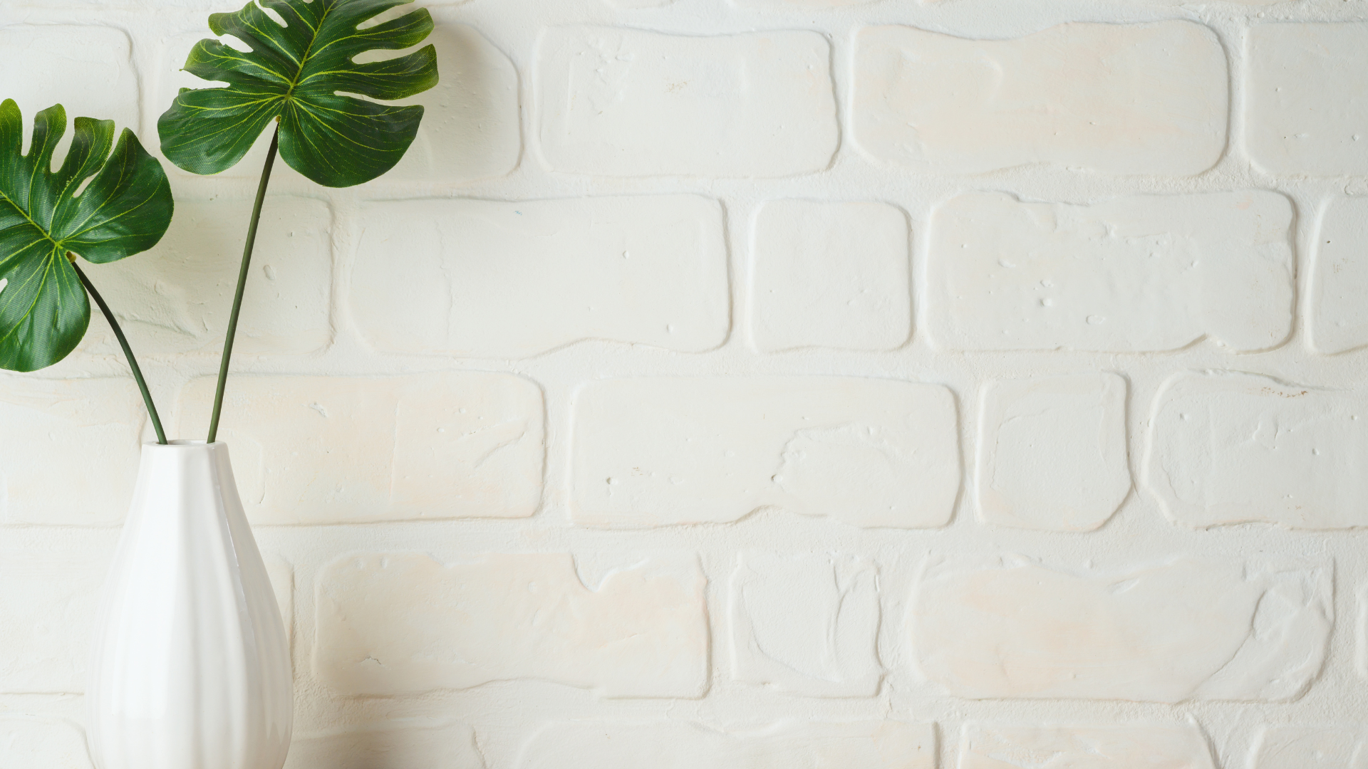 white brick wall with a white vase filled with green palm leaves